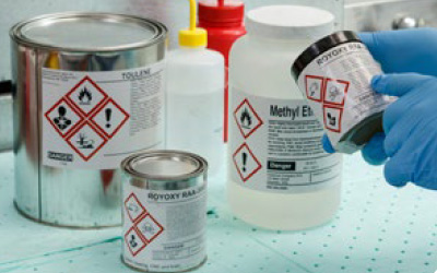 Ein Chemiker bringt ein GHS-Etikett an einem Behälter an.