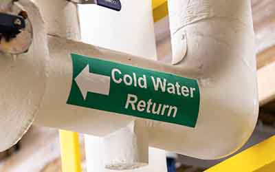 Ein Etikett mit dem Text „Cold Water Return“ (Kaltwasserrücklauf) auf einem Rohr.